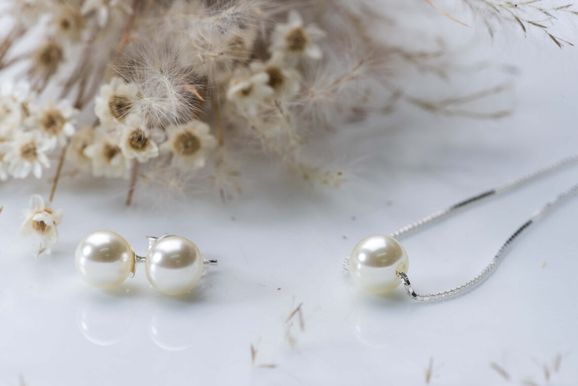 Colar de pérola com corrente de prata. Pequenas flores brancas na decoração da imagem.