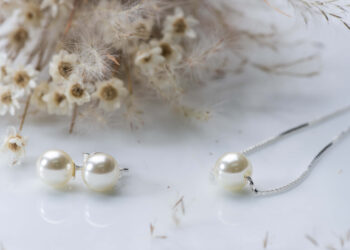 Colar de pérola com corrente de prata. Pequenas flores brancas na decoração da imagem.