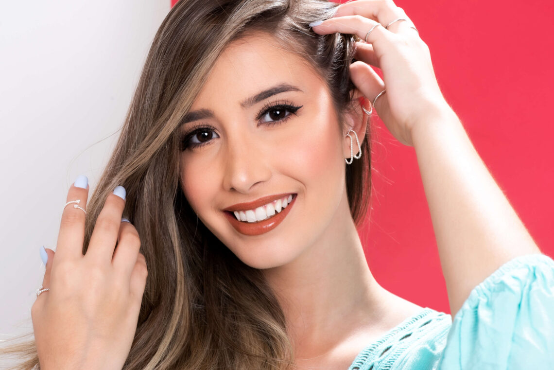 Mulher jovem e sorridente com o cabelo de lado, mostrando seus brincos ear hook prata.