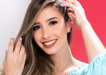 Mulher jovem e sorridente com o cabelo de lado, mostrando seus brincos ear hook prata.