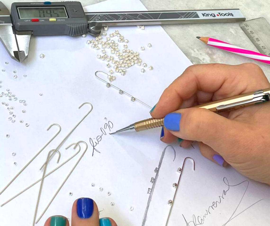Mãos femininas desenhando peças para criação de joias.