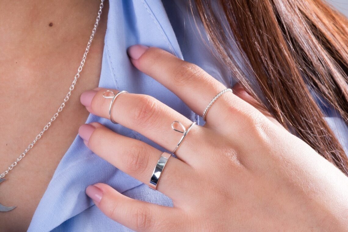 Mão esquerda feminina com diversos anéis de prata atacado.