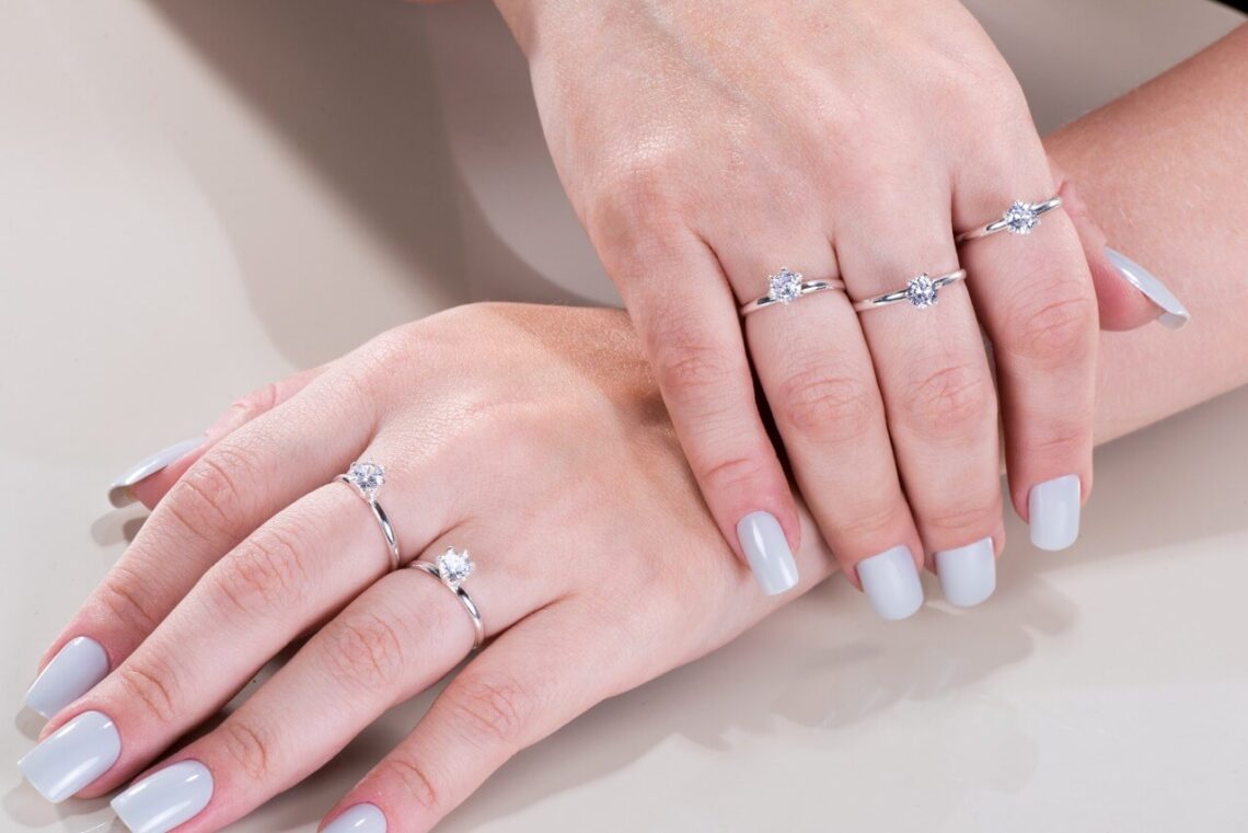 Mãos femininas utilizando diversas peças de anel solitário em seus dedos anelar, médio e indicador.